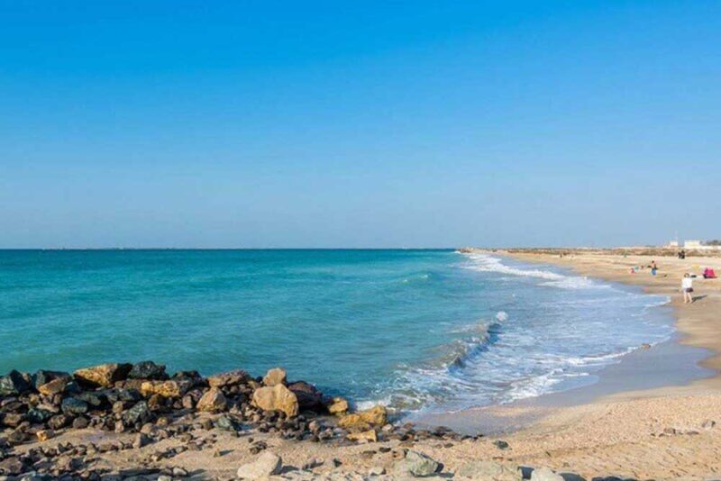 A tranquil beach in RAK with clear blue water and a rocky shoreline
