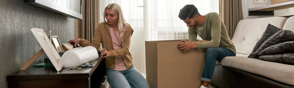 A couple unpacking boxes in their new home, carefully arranging personal items while settling in. This image could be used in a blog post for Crypto Property Finder’s Buyers and Renters guides, illustrating the moving process and making a new house feel like home.